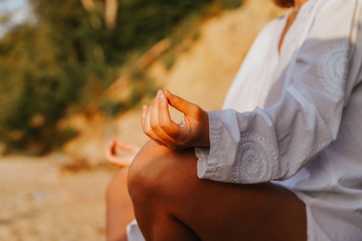 Mão em gesto de meditação sobre o joelho, luz suave do entardecer