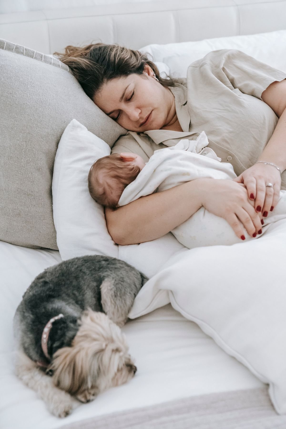 Mãe dormindo com bebê no colo, cachorro ao lado, ambiente claro e tranquilo